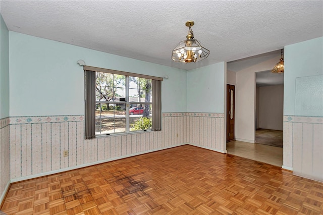 unfurnished room featuring a notable chandelier, a textured ceiling, wainscoting, baseboards, and wallpapered walls
