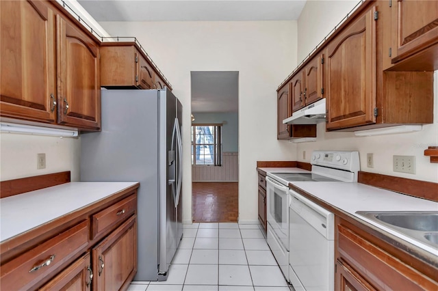 kitchen with light countertops, white appliances, brown cabinets, under cabinet range hood, and light tile patterned floors
