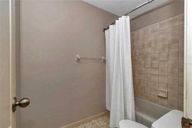 full bathroom featuring a textured ceiling, baseboards, toilet, tile patterned floors, and shower / bath combo with shower curtain