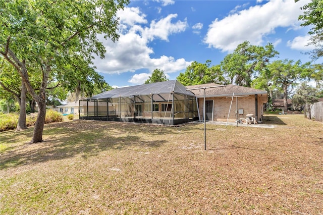 rear view of property with glass enclosure, brick siding, and a yard