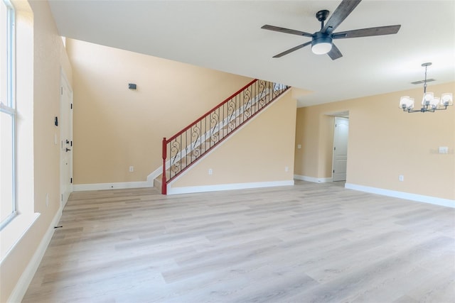 unfurnished living room with ceiling fan with notable chandelier, baseboards, light wood finished floors, and stairs