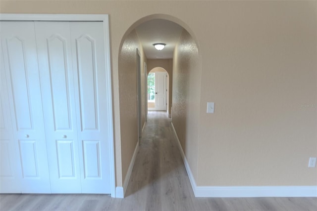 hall with arched walkways, light wood-style flooring, and baseboards