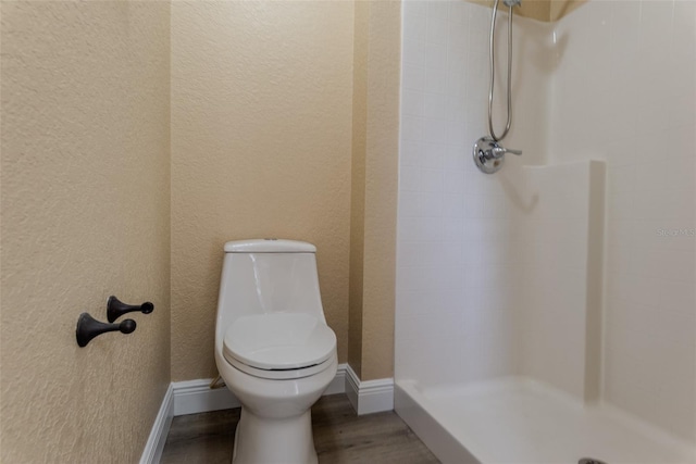 bathroom with toilet, a textured wall, wood finished floors, and a stall shower