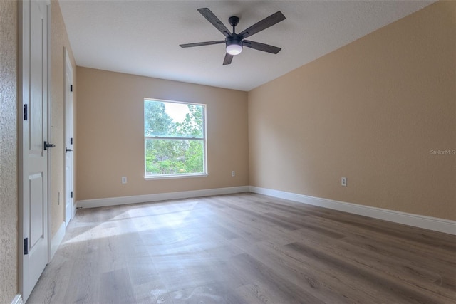 empty room featuring light wood finished floors, baseboards, and a ceiling fan