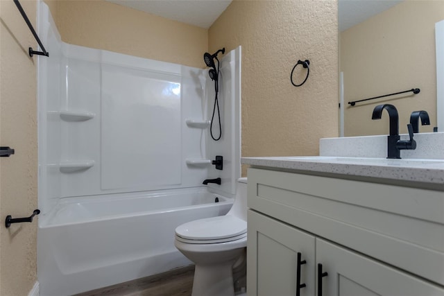 bathroom with toilet, wood finished floors, washtub / shower combination, a textured wall, and vanity