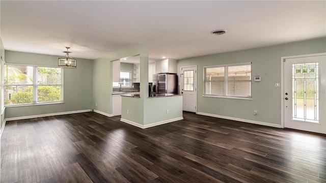 unfurnished living room featuring a wealth of natural light, dark wood-type flooring, and visible vents