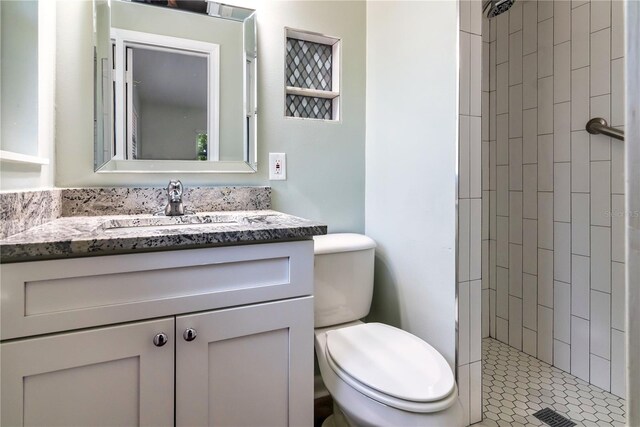 full bathroom featuring a tile shower, toilet, and vanity