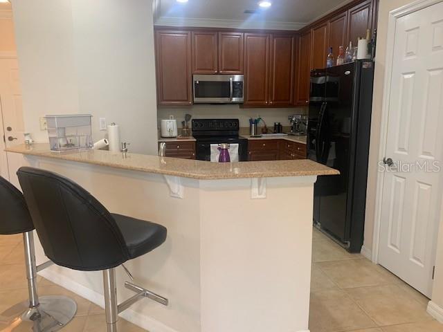 11446 Jasper Kay Ter Unit 202, Windermere, FL 34786 - kitchen with black appliances, a peninsula, a breakfast bar area, light tile patterned floors, and light countertops