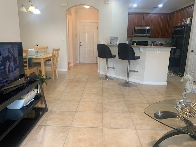 11446 Jasper Kay Ter Unit 202, Windermere, FL 34786 - kitchen with stainless steel microwave, arched walkways, a kitchen breakfast bar, refrigerator, and light tile patterned flooring