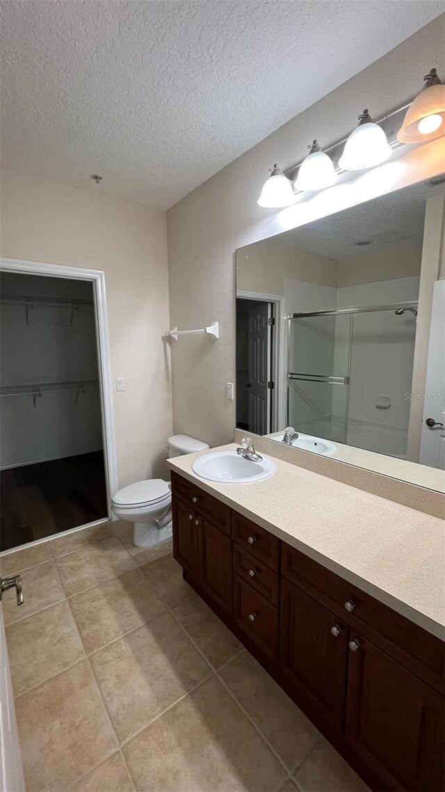 11446 Jasper Kay Ter Unit 202, Windermere, FL 34786 - bathroom featuring a stall shower, vanity, tile patterned flooring, toilet, and a textured ceiling
