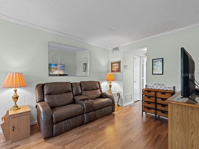 living area with a textured ceiling, ornamental molding, wood finished floors, and a wainscoted wall