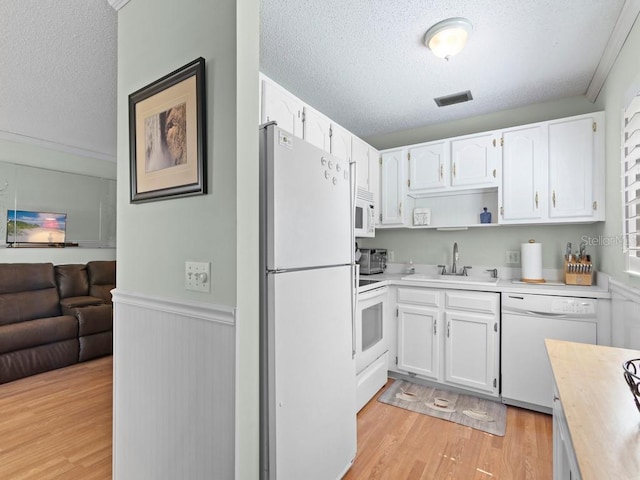 kitchen with a sink, white appliances, a textured ceiling, white cabinetry, and light countertops