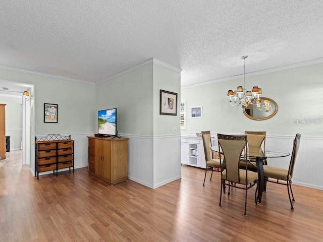 dining area with light wood-style flooring, wainscoting, ornamental molding, a chandelier, and a textured ceiling