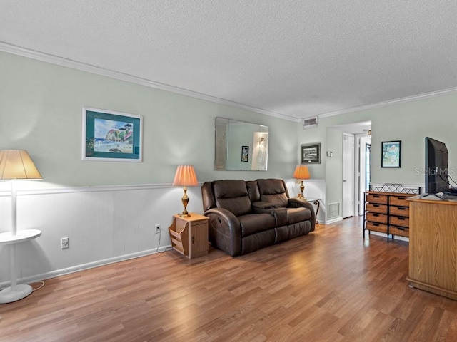living room featuring wood finished floors, a textured ceiling, ornamental molding, and a wainscoted wall