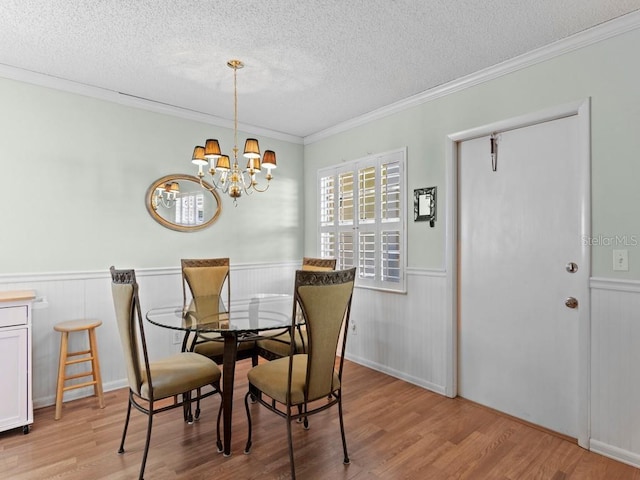 dining area with a textured ceiling, wainscoting, light wood-style flooring, a chandelier, and ornamental molding