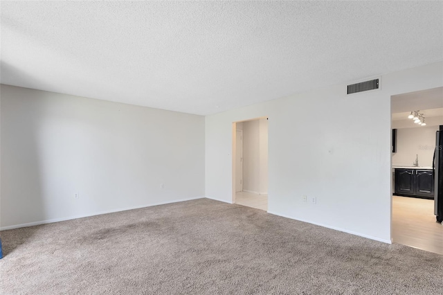 spare room with a sink, a textured ceiling, light colored carpet, and visible vents