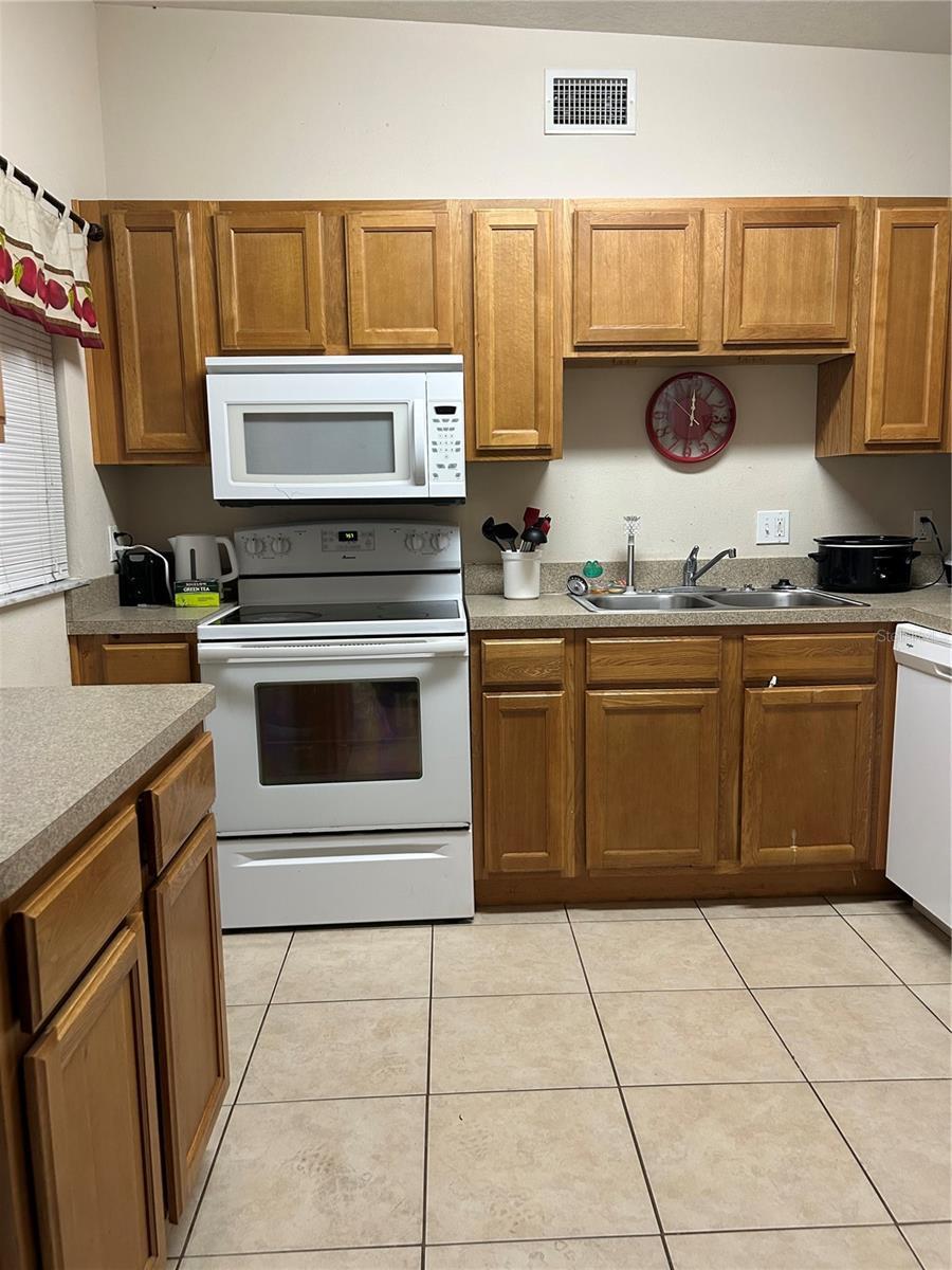 kitchen featuring visible vents, white appliances, brown cabinets, a sink, and light tile patterned floors