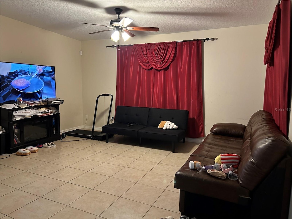 living area featuring a ceiling fan, light tile patterned floors, and a textured ceiling