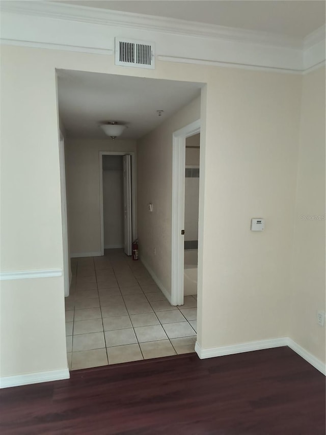 hallway with light tile patterned floors, ornamental molding, baseboards, and visible vents