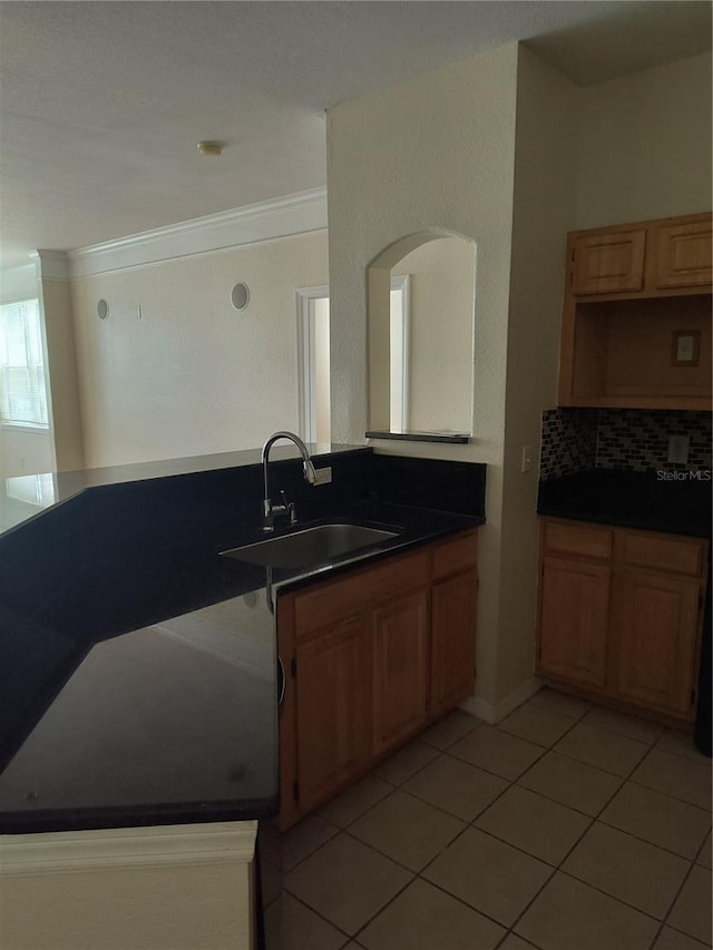 kitchen featuring light tile patterned floors, ornamental molding, backsplash, a sink, and dark countertops