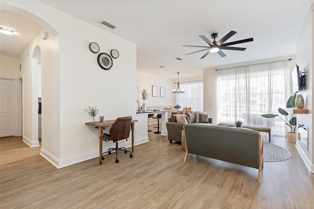 living area with light wood finished floors, arched walkways, baseboards, visible vents, and a ceiling fan