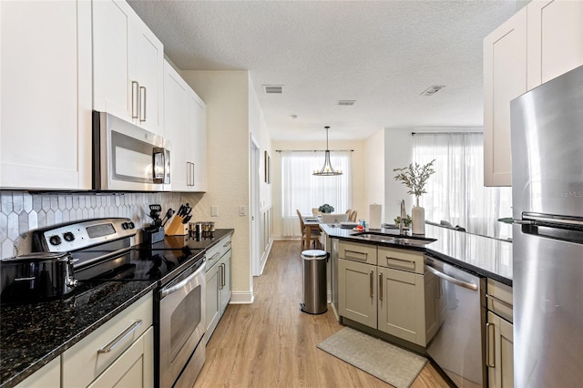 kitchen featuring stainless steel appliances, visible vents, a sink, light wood-style floors, and decorative backsplash