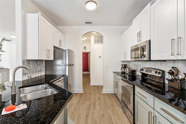 kitchen with light wood finished floors, arched walkways, a sink, tasteful backsplash, and appliances with stainless steel finishes