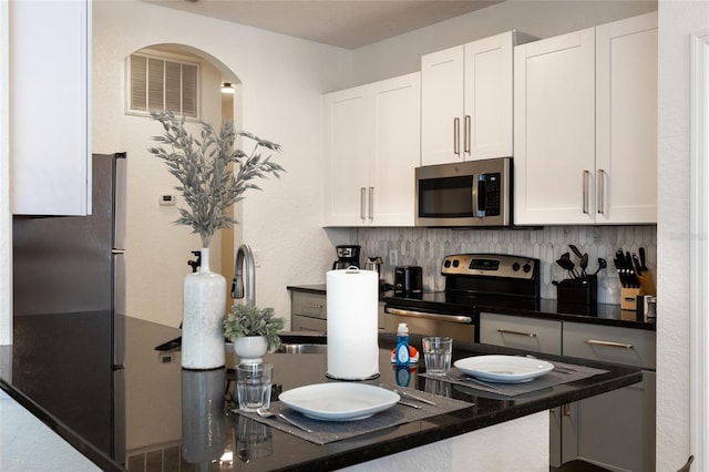 kitchen with white cabinets, stainless steel appliances, dark countertops, and tasteful backsplash