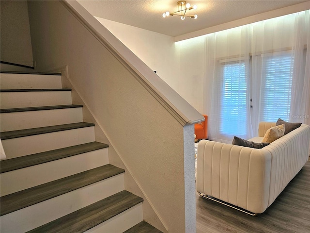 stairway with a textured ceiling, wood finished floors, and an inviting chandelier