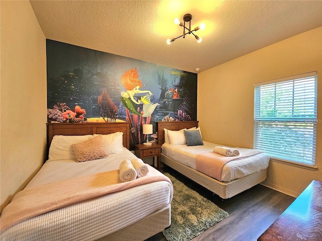 bedroom with a textured ceiling, wood finished floors, baseboards, and an accent wall