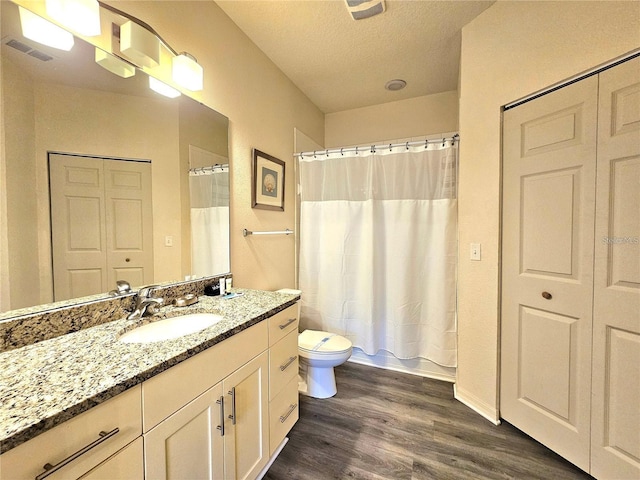 full bath with toilet, vanity, wood finished floors, a textured ceiling, and visible vents