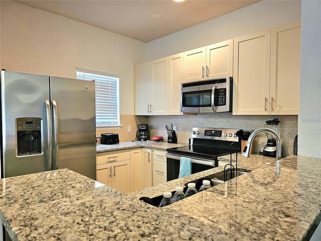 kitchen with tasteful backsplash, stainless steel appliances, a peninsula, white cabinets, and light stone countertops