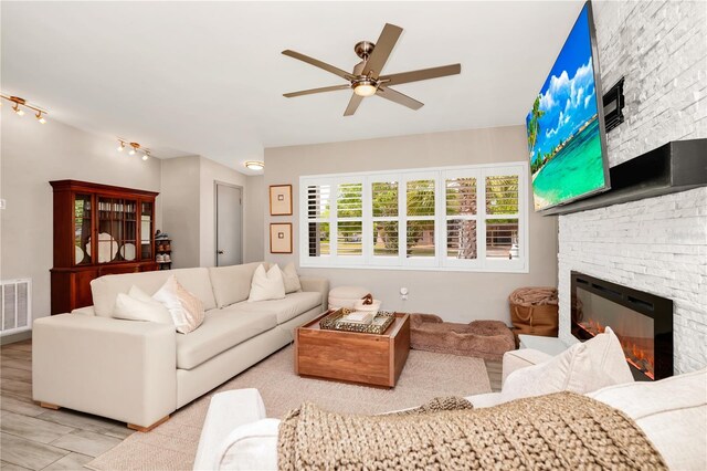living room featuring a ceiling fan, wood finished floors, a fireplace, and visible vents