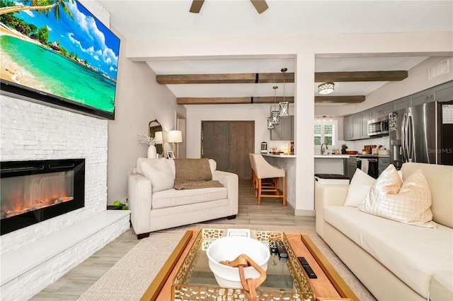 living room featuring light wood-type flooring, visible vents, beamed ceiling, and ceiling fan