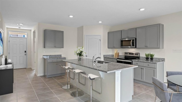 1262 Limbali St, Mount Dora, FL 32757 - kitchen with stainless steel appliances, a center island with sink, a sink, light stone counters, and gray cabinetry