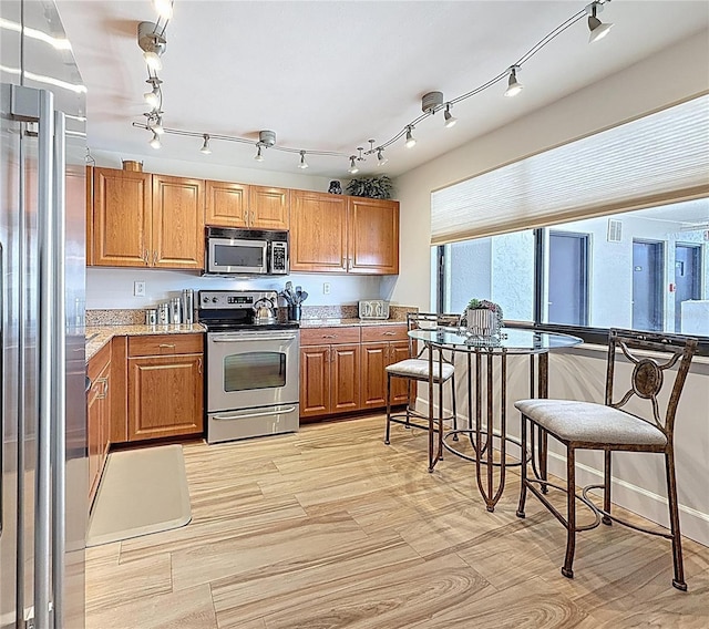 1581 Gulf Blvd Unit 102N, Clearwater Beach, FL 33767 - kitchen featuring appliances with stainless steel finishes, brown cabinets, rail lighting, and light stone counters