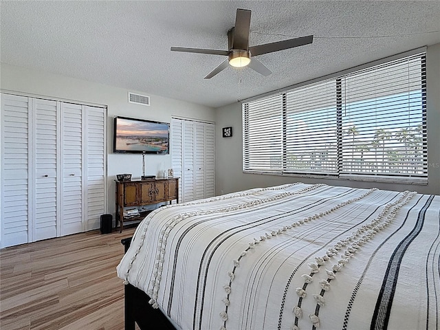 1581 Gulf Blvd Unit 102N, Clearwater Beach, FL 33767 - bedroom featuring two closets, multiple windows, light wood-style floors, a textured ceiling, and ceiling fan