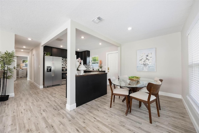 dining room with light wood finished floors, baseboards, visible vents, and a textured ceiling