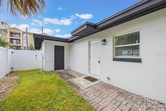 view of exterior entry featuring a gate, fence, concrete block siding, a yard, and a patio area