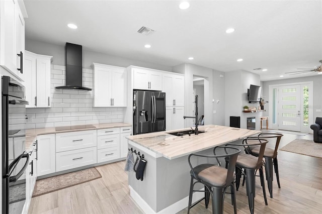 kitchen with wall chimney exhaust hood, a kitchen bar, black electric cooktop, visible vents, and fridge with ice dispenser