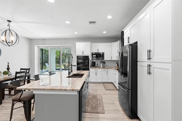 kitchen with a kitchen breakfast bar, stainless steel microwave, a sink, visible vents, and freestanding refrigerator