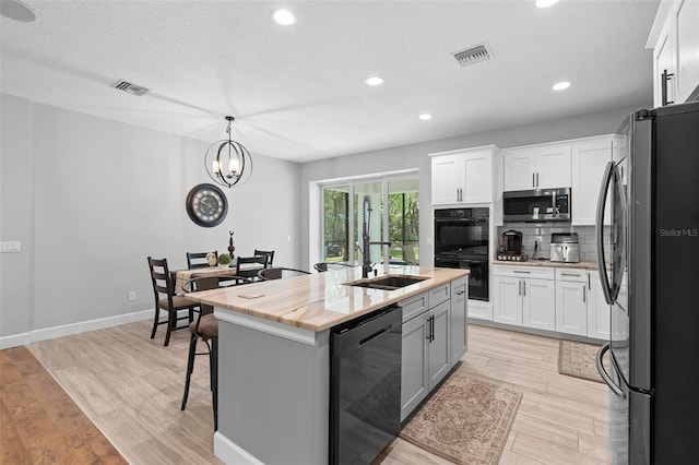 kitchen with a sink, a kitchen island with sink, black appliances, and visible vents