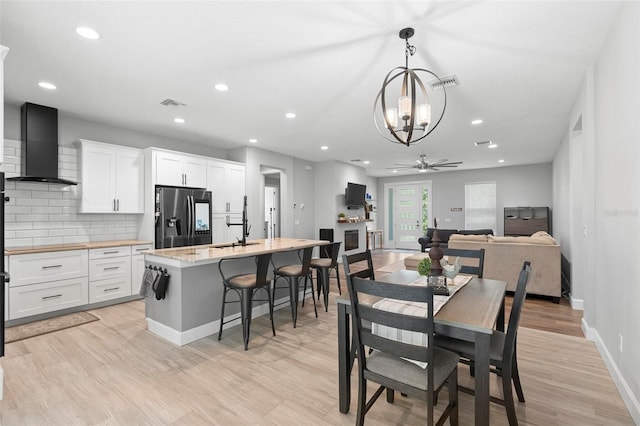 dining area featuring ceiling fan with notable chandelier, visible vents, light wood-style flooring, and baseboards
