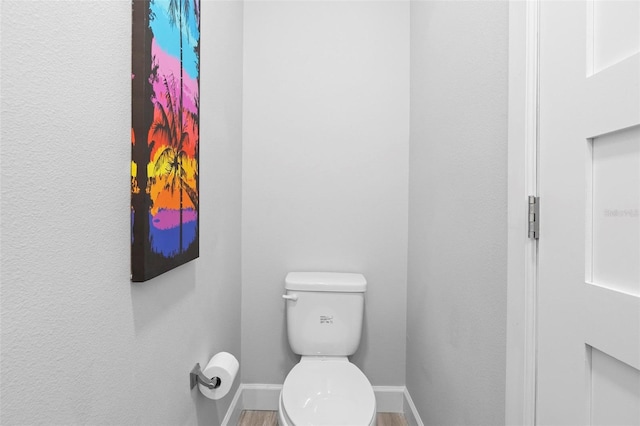 bathroom featuring baseboards, wood finished floors, and toilet