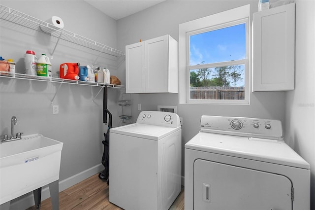 laundry room featuring baseboards, a sink, light wood finished floors, cabinet space, and washing machine and dryer