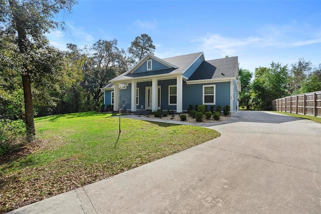 view of front facade with a front yard, covered porch, fence, and concrete driveway