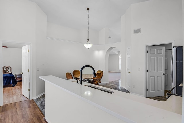 7606 Fordham Creek Ln, Orlando, FL 32818 - kitchen with arched walkways, a high ceiling, wood finished floors, hanging light fixtures, and light countertops