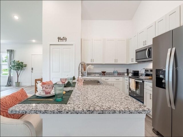 kitchen with a sink, light stone countertops, light wood-type flooring, stainless steel appliances, and white cabinets