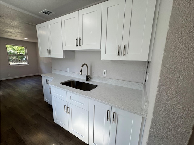 kitchen with dark wood-type flooring, visible vents, white cabinetry, and a sink