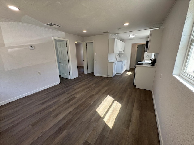 unfurnished living room featuring visible vents, recessed lighting, a sink, baseboards, and dark wood-style floors
